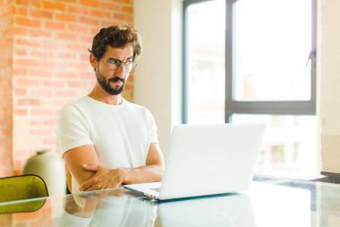 Dizüstü bilgisayarı olan genç sakallı bir adam üzgün, üzgün ya da kızgın. Olumsuz bir tavırla yan yana bakıyor, anlaşmazlık içinde kaşlarını çatıyor.