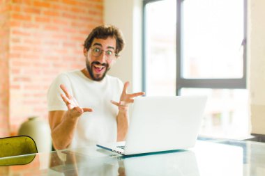 Dizüstü bilgisayarı olan genç sakallı adam kendini mutlu, şaşkın, şanslı ve şaşırmış hissediyor. İnanılmaz!