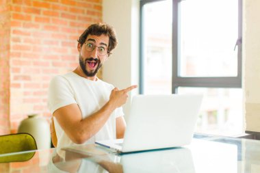 Dizüstü bilgisayarı olan genç sakallı adam heyecanlı ve şaşırmış görünüyor.