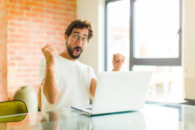 Dizüstü bilgisayarı olan genç sakallı bir adam inanılmaz bir başarıyı kutluyor. Kazanan gibi, heyecanlı ve mutlu görünüyor.!