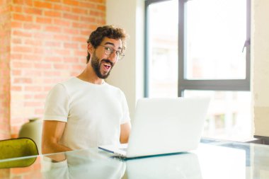 Dizüstü bilgisayarı olan genç sakallı bir adam. Büyük, dostane, kaygısız bir gülümsemesi var. Olumlu, rahat ve mutlu görünüyor.