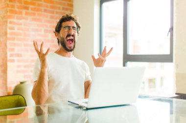 Dizüstü bilgisayarı olan genç sakallı bir adam öfkeyle bağırıyor, stresli ve elleri havada neden benim...