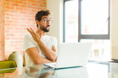 Dizüstü bilgisayarı olan genç sakallı bir adam kafası karışık ve habersiz, şüpheli bir açıklama ya da düşünce hakkında merak ediyor.