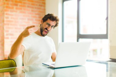 Bilgisayarlı genç sakallı bir adam kızgın agresif bir ifadeyle kameraya bakıyor. Öfkeli, çılgın bir patron gibi görünüyor.