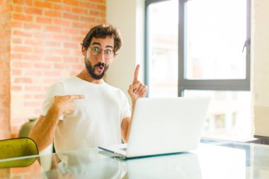 Dizüstü bilgisayarı olan genç sakallı bir adam gururlu ve şaşırmış hissediyor. Kendine güvenerek kendini bir numara gibi hissediyor.