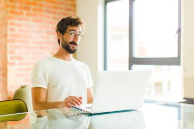 Dizüstü bilgisayarı olan genç sakallı bir adam kafası karışık ve şüpheli hissediyor, merak ediyor ya da karar vermeye çalışıyor.