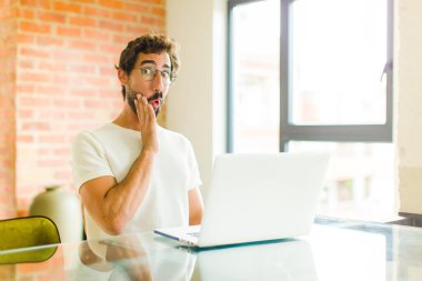 Dizüstü bilgisayarı olan genç sakallı bir adam şok olmuş ve ağzı açık bir şekilde yüz yüze inanamamaktan hayrete düşmüş.