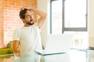 Dizüstü bilgisayarı olan genç sakallı bir adam neşeli ve sıradan bir şekilde gülümsüyor, pozitif, mutlu ve kendinden emin bir bakışla kafa kafaya gidiyor.