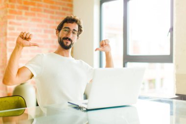 Dizüstü bilgisayarı olan genç sakallı bir adam gururlu, kibirli ve kendinden emin, tatmin olmuş ve başarılı görünüyor.