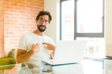 Dizüstü bilgisayarı olan genç sakallı bir adam şaşkın ve tuhaf bakışlarıyla kendini işaret ediyor. Seçildiğine şaşırmış ve şaşırmış.