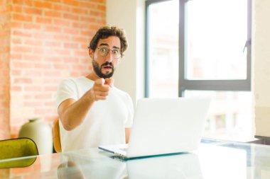 Dizüstü bilgisayarı olan genç sakallı bir adam şok olmuş ve şaşırmış hissediyor. Şaşırmış ve ağzı açık bir şekilde hayranlıkla yukarı bakıyor.