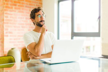 Dizüstü bilgisayarı olan genç sakallı bir adam düşünceli, meraklı ya da hayal kuran, hayal kuran ve uzayı kopyalamak isteyen biri.