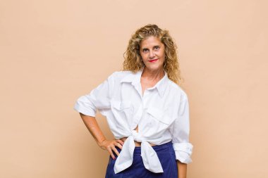 Orta yaşlı bir kadın mutlu bir şekilde gülümsüyor. Kendine güvenen, olumlu, gururlu ve arkadaş canlısı bir tavırla.