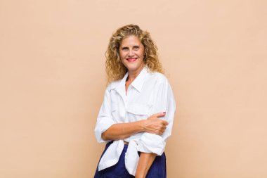 Orta yaşlı bir kadın utangaç ve neşeli bir şekilde gülüyor, arkadaş canlısı ve olumlu ama güvensiz bir tavırla.