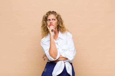 Orta yaşlı bir kadın mutlu bir şekilde gülümsüyor ve hayal kuruyor ya da şüphe ediyor.