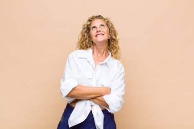 Orta yaşlı bir kadın mutlu, gururlu ve umutlu, merak ediyor ya da düşünüyor, çapraz kollarla fotokopi çekmeyi bekliyor.