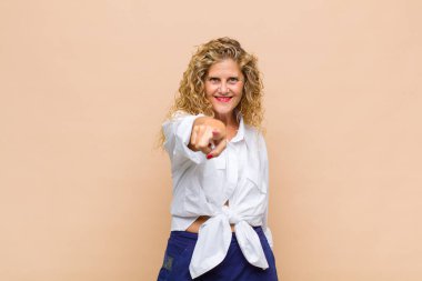 Orta yaşlı bir kadın kameraya bakıyor, kendinden emin, arkadaş canlısı bir gülümsemeyle, seni seçiyor.