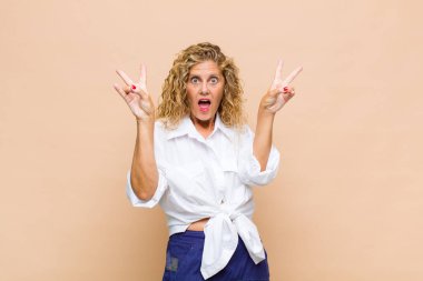 Orta yaşlı kadın gülümsüyor ve mutlu görünüyor, arkadaş canlısı ve memnun, zafer ya da barış işareti yapıyor iki eliyle