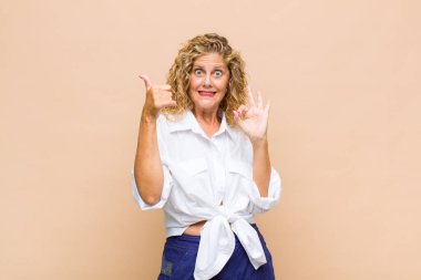 Orta yaşlı bir kadın mutlu, şaşkın, tatmin olmuş ve şaşırmış hissediyor, iyi görünüyor ve el kol hareketleri yapıyor, gülümsüyor.