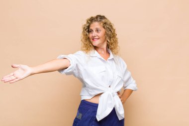 Orta yaşlı bir kadın kendini mutlu ve neşeli hissediyor, gülümsüyor ve seni hoş karşılıyor, dostça bir jestle içeri davet ediyor.