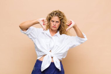 Orta yaşlı bir kadın üzgün, hayal kırıklığına uğramış ya da kızgın görünüyor. Anlaşmazlıkta baş parmağını gösteriyor. Hayal kırıklığına uğramış hissediyor.