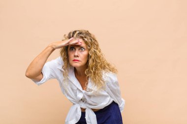 Orta yaşlı kadın şaşkınlık ve şaşkınlık içinde bakıyor. Alnı açık, uzaklara bakıyor, izliyor ya da arıyor.