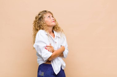 Orta yaşlı bir kadın omuz silkiyor, kafası karışık ve kararsız, kolları bağlı ve şaşkın görünüyor.