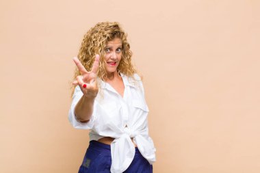 Orta yaşlı bir kadın gülümsüyor ve arkadaş canlısı görünüyor. İki ya da iki numarayı gösteriyor. Elleri önde, geriye doğru sayıyor.