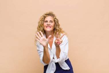 Orta yaşlı bir kadın gülümsüyor ve dost canlısı görünüyor, 7 ya da 7 numarayı gösteriyor, eli önde, geriye doğru sayıyor.