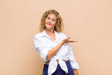 Orta yaşlı bir kadın neşeli bir şekilde gülümsüyor, mutlu hissediyor ve fotokopi alanında bir konsept gösteriyor.