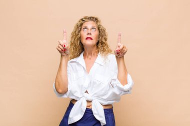 Orta yaşlı bir kadın şaşırmış, şaşırmış ve ağzı açık bir şekilde iki elini de havaya kaldırıp boşluğu dolduruyor.