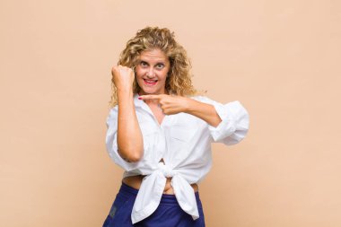 Orta yaşlı bir kadın sabırsız ve kızgın görünüyor, saati gösteriyor, dakiklik istiyor, zamanında gelmek istiyor.