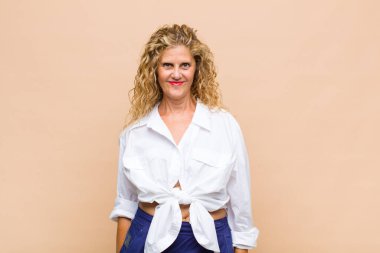 Orta yaşlı kadın pozitif ve kendinden emin gülümsüyor. Tatmin olmuş, arkadaş canlısı ve mutlu görünüyor.