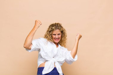 Orta yaşlı bir kadın muzaffer bir şekilde bağırıyor, heyecanlı, mutlu ve şaşırmış görünüyor, kutlama yapıyor.