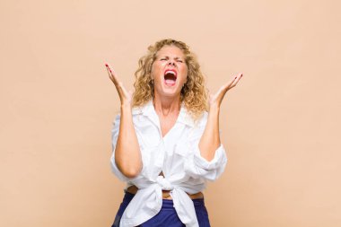 Orta yaşlı bir kadın öfkeyle bağırıyor, stresli hissediyor ve ellerini havaya kaldırıp neden ben diye bağırıyor.