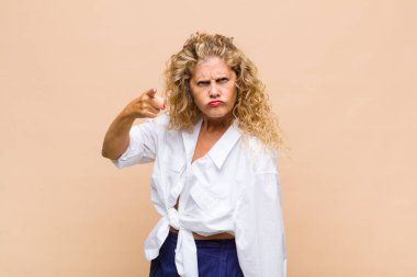 Orta yaşlı bir kadın kızgın agresif bir ifadeyle kameraya bakıyor. Öfkeli, deli bir patron gibi görünüyor.