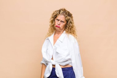 Orta yaşlı bir kadın üzgün ve mızmızlanıyor, mutsuz bir bakışla, negatif ve hayal kırıklığına uğramış bir tavırla ağlıyor.