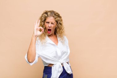 Orta yaşlı bir kadın kendini başarılı ve tatmin olmuş hissediyor ağzı açık gülümsüyor, elle işaret veriyor.