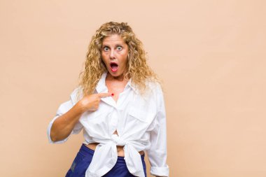 Orta yaşlı kadın şok olmuş ve şaşırmış görünüyor ağzı açık, kendini işaret ediyor.