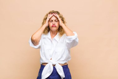 Orta yaşlı bir kadın stresli ve endişeli, depresif ve hayal kırıklığına uğramış hissediyor, iki elini de başa kaldırıyor.