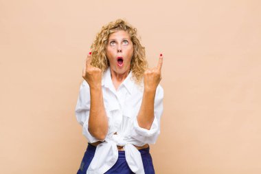 Orta yaşlı bir kadın şaşırmış ve ağzı açık bir şekilde şaşkın ve şaşkın bir bakışla yukarı bakıyor.