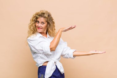 Orta yaşlı bir kadın bir objeyi iki eliyle fotokopi alanında tutuyor, bir objeyi gösteriyor, sunuyor ya da reklamını yapıyor.