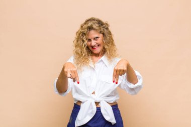 Orta yaşlı, ağzı açık bir kadın iki eliyle aşağıya doğru bakıyor, şaşkın, şaşkın ve şaşırmış görünüyor.