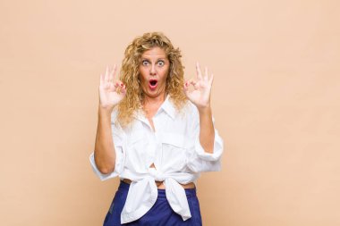 Orta yaşlı kadın şok olmuş, şaşırmış ve şaşırmış hissediyor. Onaylıyor. İki eliyle de onay işareti yapıyor.