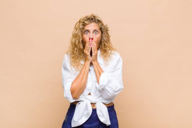 Orta yaşlı bir kadın endişeli, üzgün ve korkmuş hissediyor, elleriyle ağzını kapatıyor, endişeli ve berbat görünüyor.