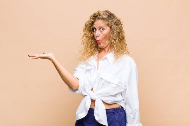 Orta yaşlı kadın şaşırmış ve şoka uğramış görünüyor, çenesi düşmüş ve eli açık bir nesneyi tutuyor.