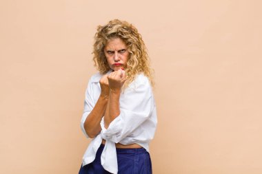 Orta yaşlı kadın kendinden emin, sinirli, güçlü ve agresif görünüyor. Yumrukları boks pozisyonunda dövüşmeye hazır.