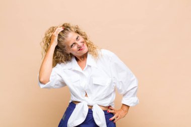 Orta yaşlı bir kadın neşeli ve tesadüfen gülümsüyor, olumlu, mutlu ve kendinden emin bir bakışla göğüs göğüse tutuşuyor.