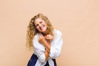 Orta yaşlı bir kadın neşeli bir şekilde gülümsüyor ve yumruklarını sıkmış, kollarını kavuşturmuş, mutlu ve pozitif hissediyor.