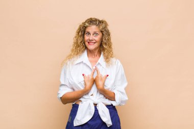 Orta yaşlı bir kadın, şaşkın ve tuhaf bakışlarıyla kendini işaret ediyor. Seçildiğine şaşırmış ve şaşırmış.